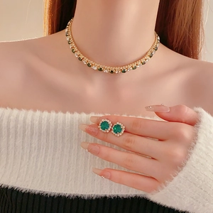 Close-up of gold necklace and earrings set with green round gemstones and diamonds