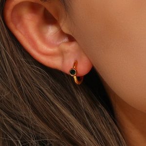 Close-up of a 18K gold plated earring with a round deep green zircon on a model