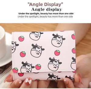 Pink trifold mini wallet with cute cow and strawberry prints shown in hands on a desk