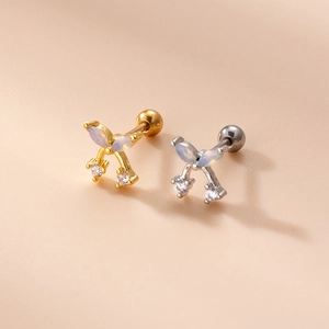 Close-up of gold and silver bow cartilage earrings with opal wings and cubic zirconia drop
