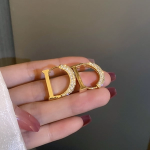 Détail de boucles d'oreilles créoles lettre D dorées avec pavé de zircons brillants