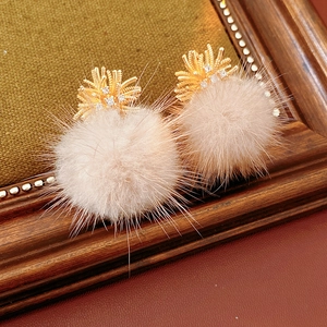 Close-up of golden earrings with zircon top and large light pink fluffy fur balls