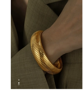 Detail of wide golden ribbed cuff bracelet on wrist showing metallic texture and luster