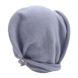 Close-up of grey-blue knit beanie featuring a delicate golden heart-shaped metal pin detail