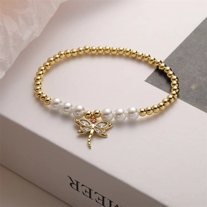 Macro shot of gold-plated dragonfly charm with clear zircons and red gemstone accents