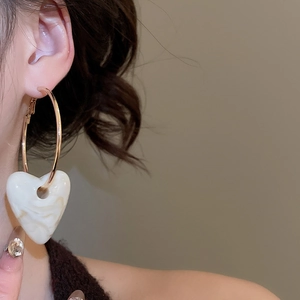 Detailed close-up of a large gold hoop earring with a textured white heart pendant on a model