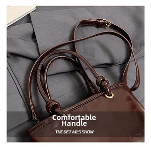 Détail du cabas en cuir poli marron foncé avec poignées rondes et accents noués élégants