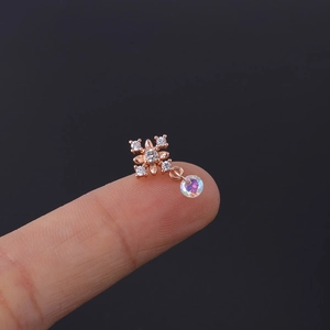 Close-up of rose gold flower earring with sparkling zircon and colorful bead on fingertip
