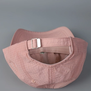 Close-up of the adjustable metal buckle strap on a light pink checkered baseball cap