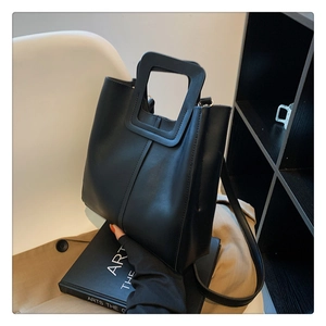 Dettaglio di una borsa tote nera minimalista con un manico quadrato ritagliato su libri d'arte