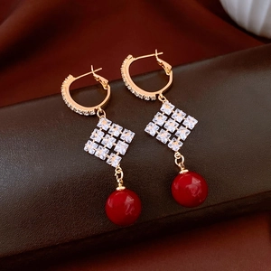Détail de boucles d'oreilles dorées 18k avec losange en diamant et perle rouge