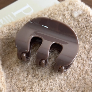 Detail view of brown acrylic M-shaped hair claw clip on soft plush fabric background