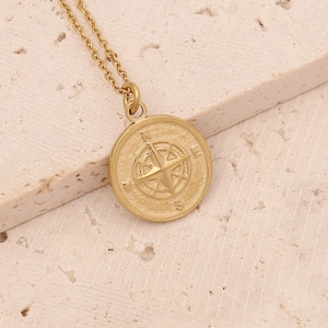 Detailed close-up of golden compass pendant necklace with N S E W engravings on stone
