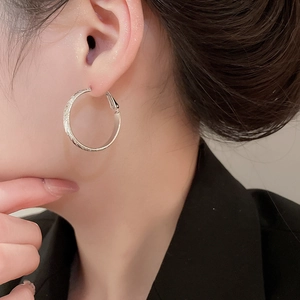 Close-up of elegant silver textured hoop earring on model showing fine metallic detail
