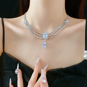 Detail of silver teardrop necklace with zircon crystals worn by a model on black background