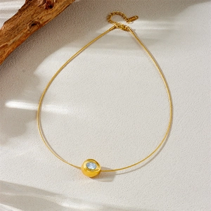 Gold-plated stainless steel necklace with round blue gemstone pendant on beige texture