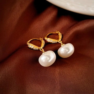 Vue macro de boucles d'oreilles dorées avec diamants pavés et perles blanches