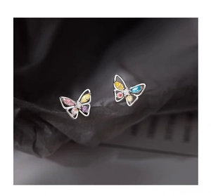 Macro shot of silver butterfly stud earrings with colorful zircon stones on grey background