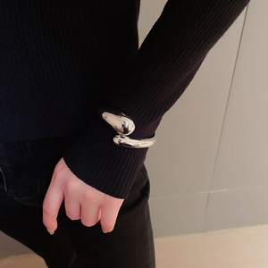 Close-up of polished silver teardrop open bangle worn over a black knit sleeve
