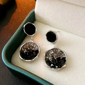 Gros plan de boucles d'oreilles géométriques en argent avec cristaux sombres en boîte