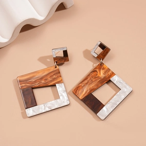 Detail of tortoiseshell and white resin geometric earrings on warm beige background