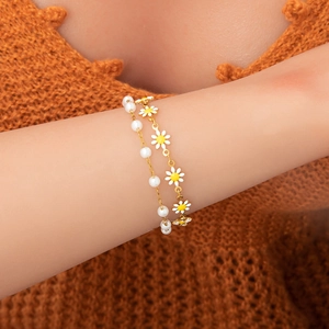Gros plan d'un bracelet doré double couche avec perles blanches et breloques marguerite