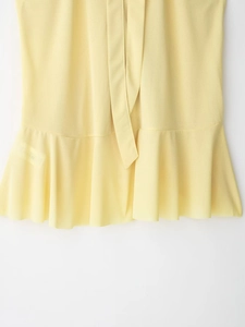 Detail of light yellow halter top featuring pleated hem and crepe fabric texture