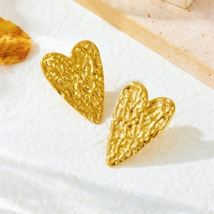 Detail of golden heart-shaped drop earrings with hammered texture on a natural stone base