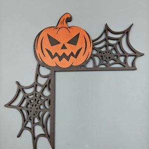 Close-up of laser-cut wooden Halloween door corner decor featuring pumpkin and spider webs