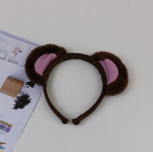 Detail view of plush brown monkey ears headband with pink inner lining on a flat surface