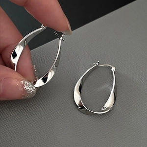 Detailed view of silver oval hoop earrings with a twisted design held in hand for scale
