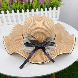 Detail of wide brim straw sun hat featuring black bow and champagne leaf embroidery