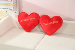 Detail of red plush heart pillows with I Love You gold embroidery on a cozy sofa
