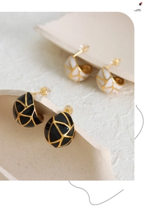 Macro shot of gold-plated geometric C-shaped earrings with black and white enamel details