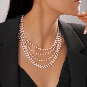 Detail of four-layer faux pearl necklace with gold links worn by a model in black attire