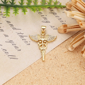 Macro detail of golden Caduceus medical pendant with zircon wings on vintage paper