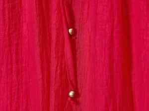 Détail de la texture en crêpe rouge avec perles dorées décoratives sur le cordon