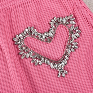 Detail aus rosa Plissee-Stoff mit herzförmigen Strass-Verzierungen und Textur