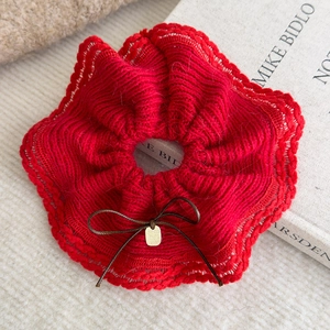 Close-up of red knit scrunchie with bow and gold tag on soft beige texture
