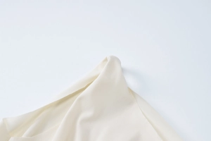 Detail of a cream one-shoulder dress showing seamless neckline and smooth fabric texture