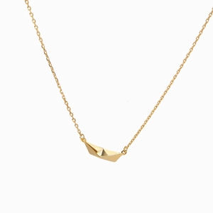 Macro detail of a golden origami boat pendant on a delicate minimalist chain necklace