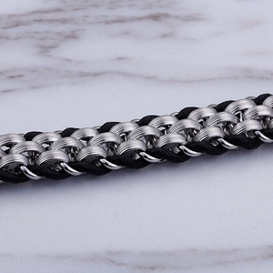 Detail of silver wolf-head clasp and black braided leather cord texture on a marble surface