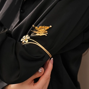 Detail of gold butterfly and flower open cuff bracelet worn over black sleeve clothing