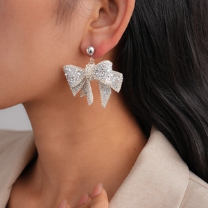 Close-up detail of silver bow earrings with micro-pave crystals on female model