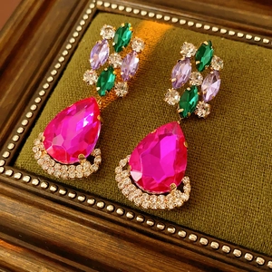 Detail of vintage rhinstone earrings featuring a large pink pear-cut stone on green velvet
