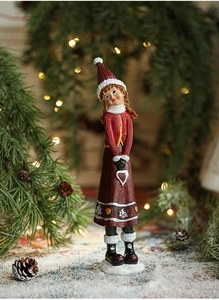 Close-up of a resin Christmas girl figurine in red knit dress among snowy pine branches