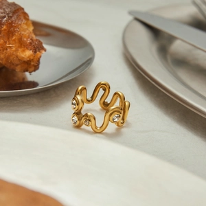 Bague dorée ondulée avec zircons incrustés sur une surface en pierre au style épuré