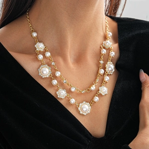 Detail van een dubbele gouden halsketting met witte parels en glinsterende strass-bloemen
