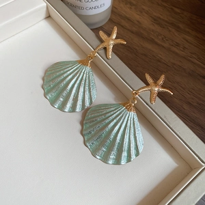 Detailed close-up of mint green shell drop earrings with golden starfish studs