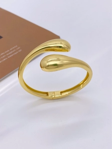 Macro detail of gold teardrop cuff bracelet showing mirrored finish and open design